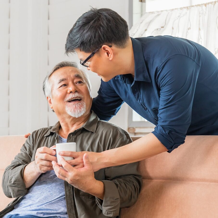 man-cargiving-for-father man handing tea to father while providing financial planning.